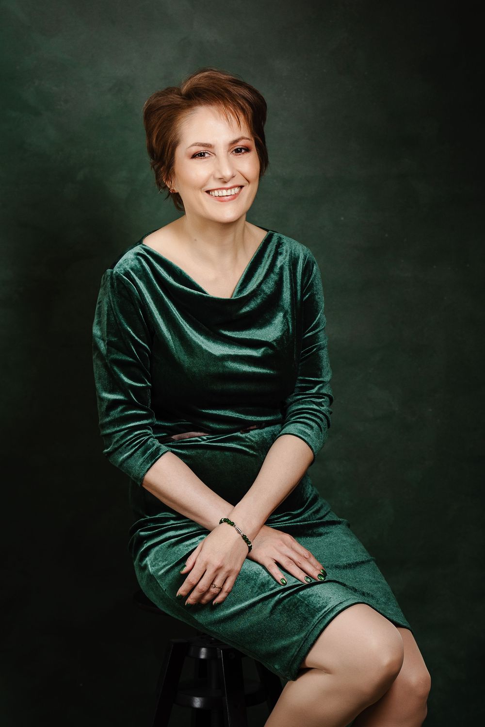 Portrait series in emerald green velvet dress against dark background showing elegant seated poses.
