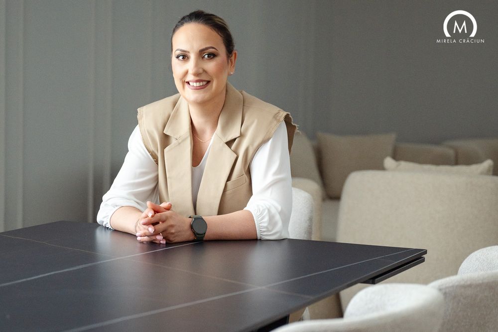Professional in beige vest and white blouse sits at dark table in modern office interior with neutral decor.