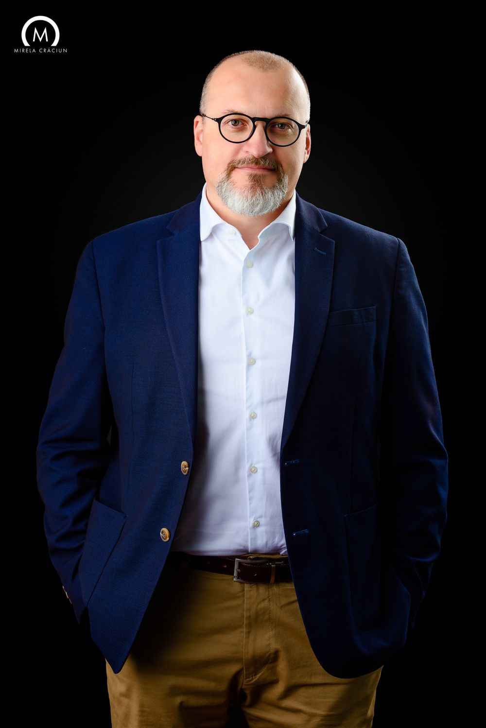 Professional headshot against black background featuring navy blazer and white shirt.