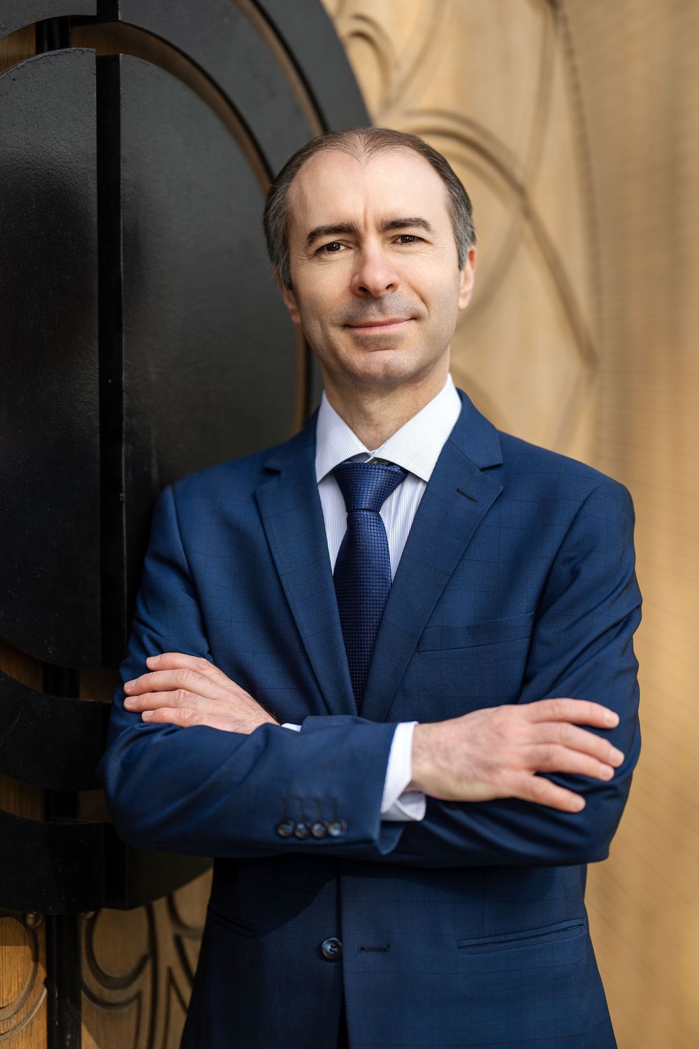 Professional portrait series showing a person in a navy suit with crossed arms against a neutral background.