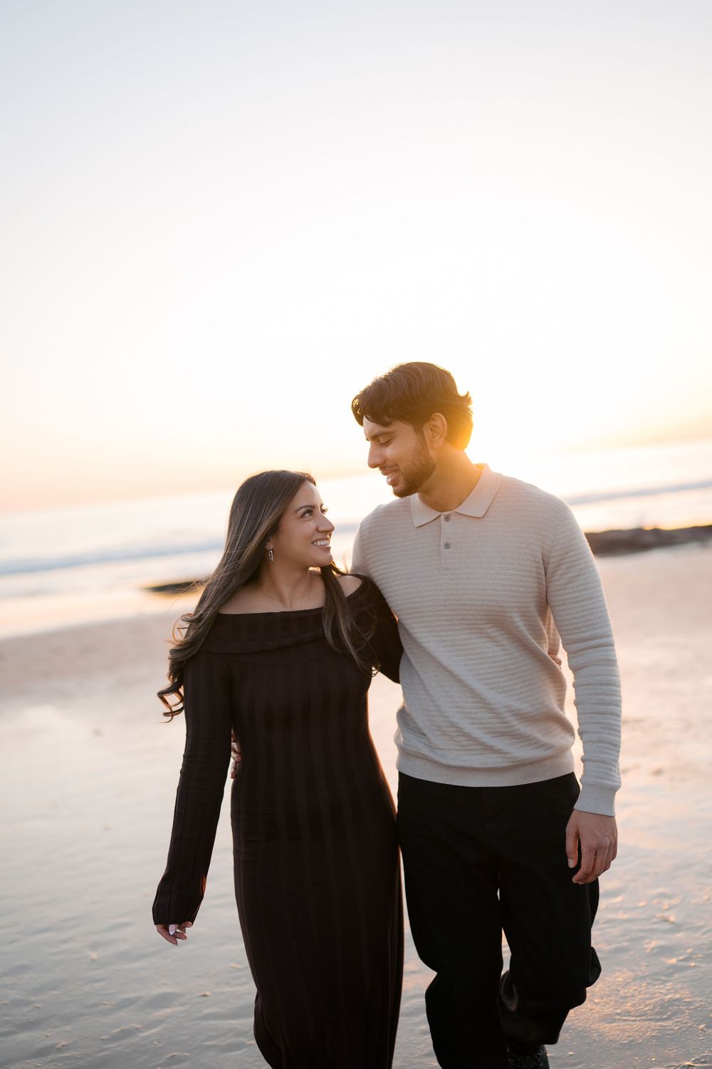 A couple shares a joyful moment together on the beach at sunset with golden light illuminating their smiles.