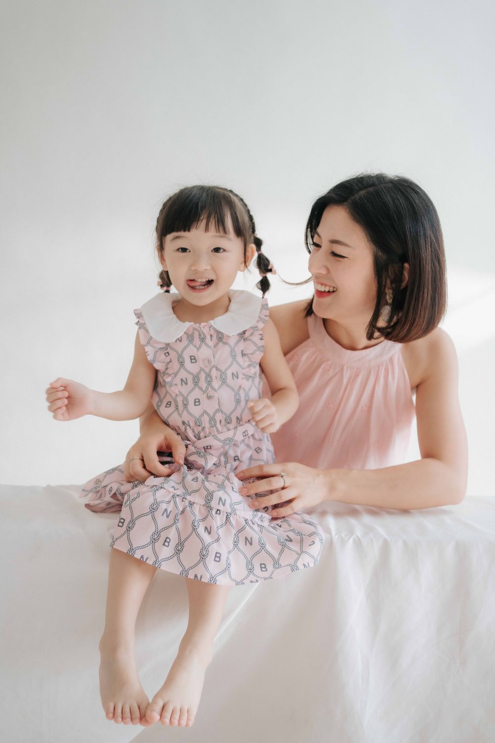 A parent and baby in matching pink outfits share joyful moments together against a white backdrop in a photo series.