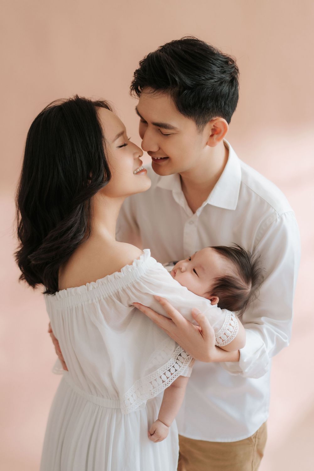 A romantic couple in white outfits share tender moments in a series of intimate portraits against a soft pink background.