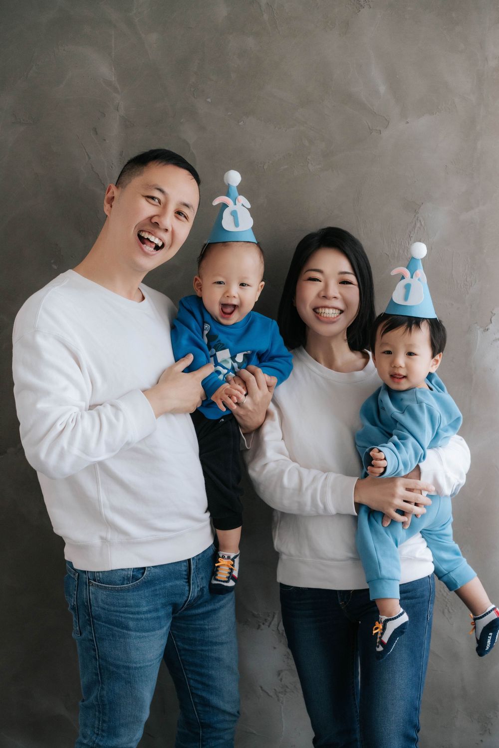 A family wearing matching white and denim outfits poses together against a gray wall in a playful photo series.