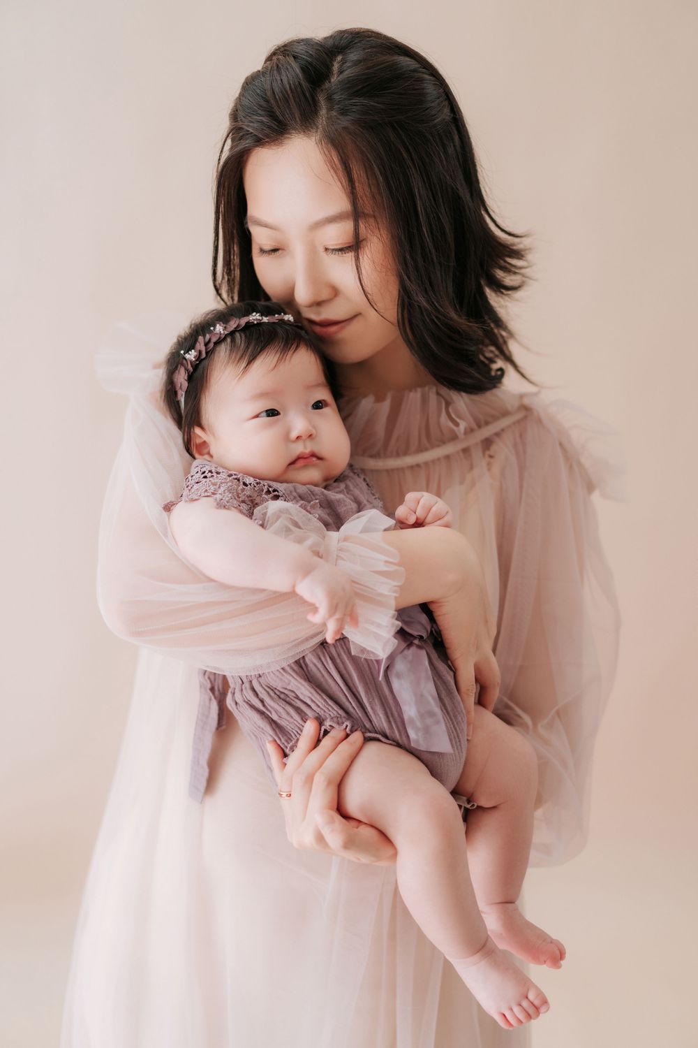 A parent and baby share tender moments together in soft pink tones during an intimate portrait session.