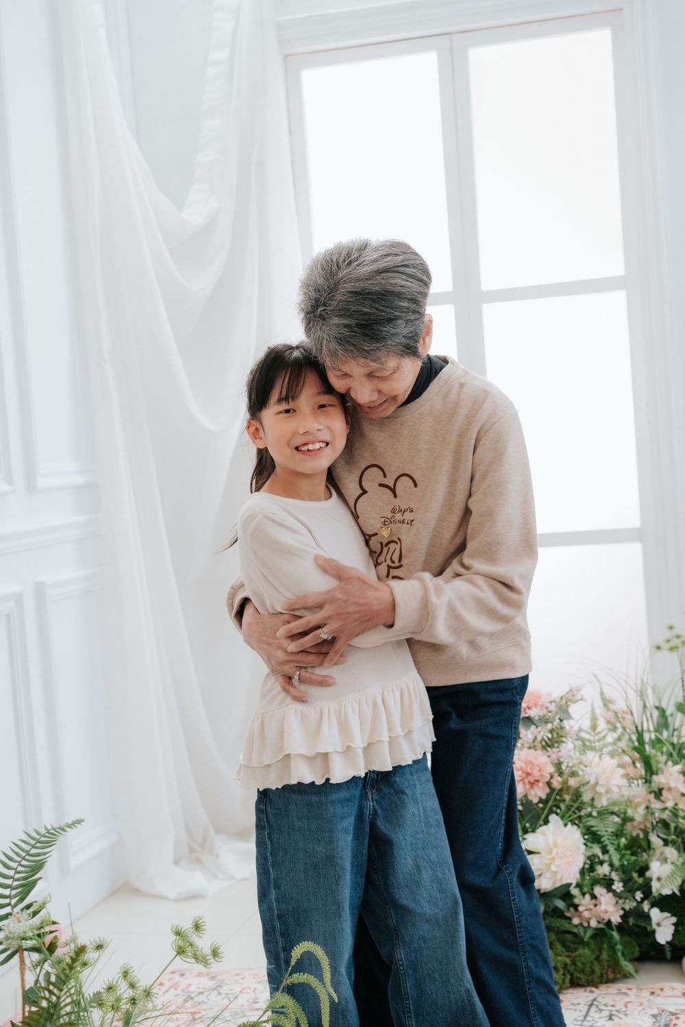 Heartwarming family moment in a bright white room with soft natural light and potted plants by the window.