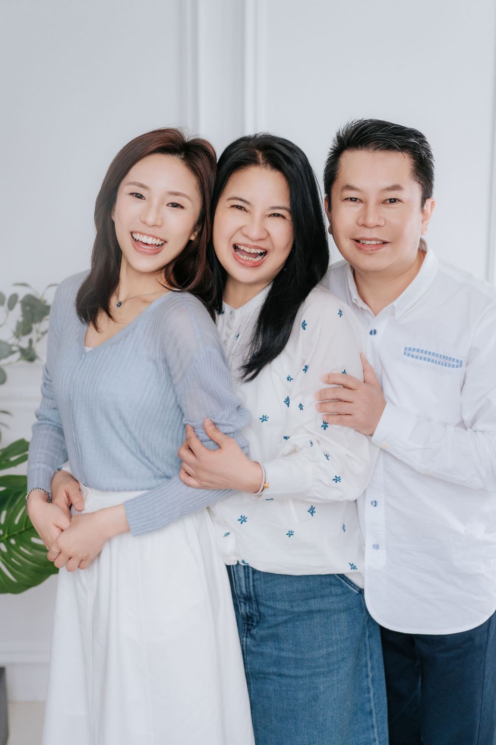 Three people wearing coordinated blue and white outfits pose together in a bright studio setting.