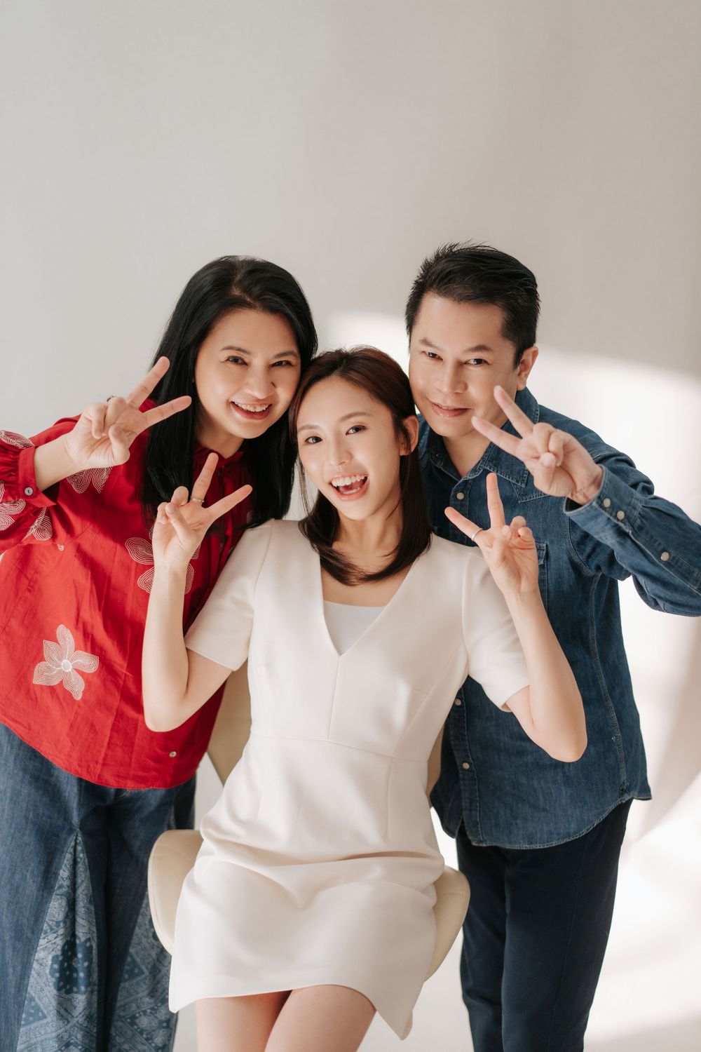A joyful group in casual outfits poses playfully together against a white wall in a photo series.