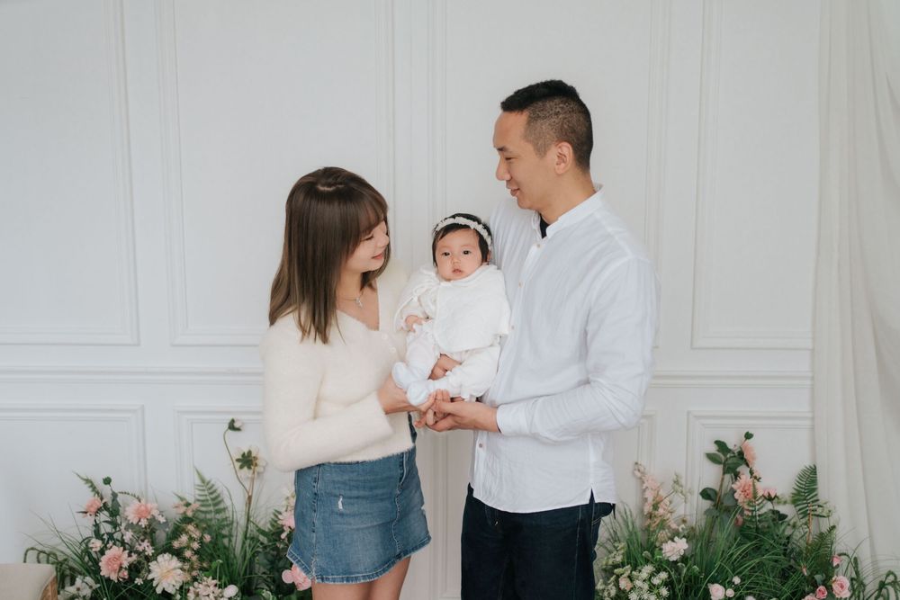 A family in white and denim outfits poses together against a light wall with pink floral decorations.