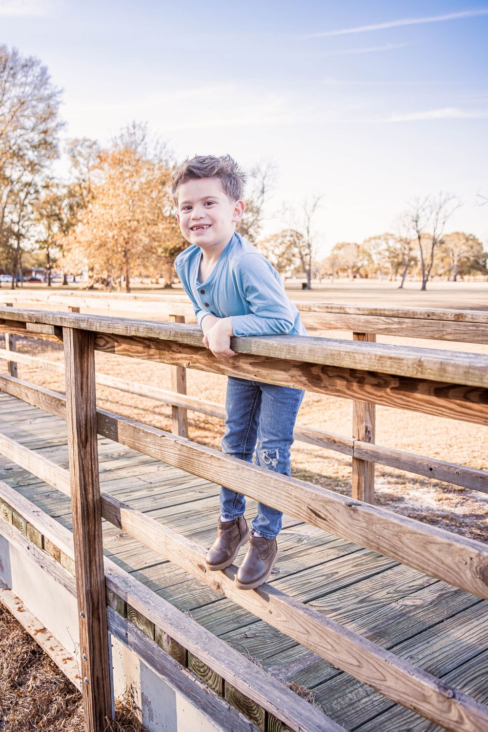 A child plays and balances on a wooden bridge railing in a park during autumn.