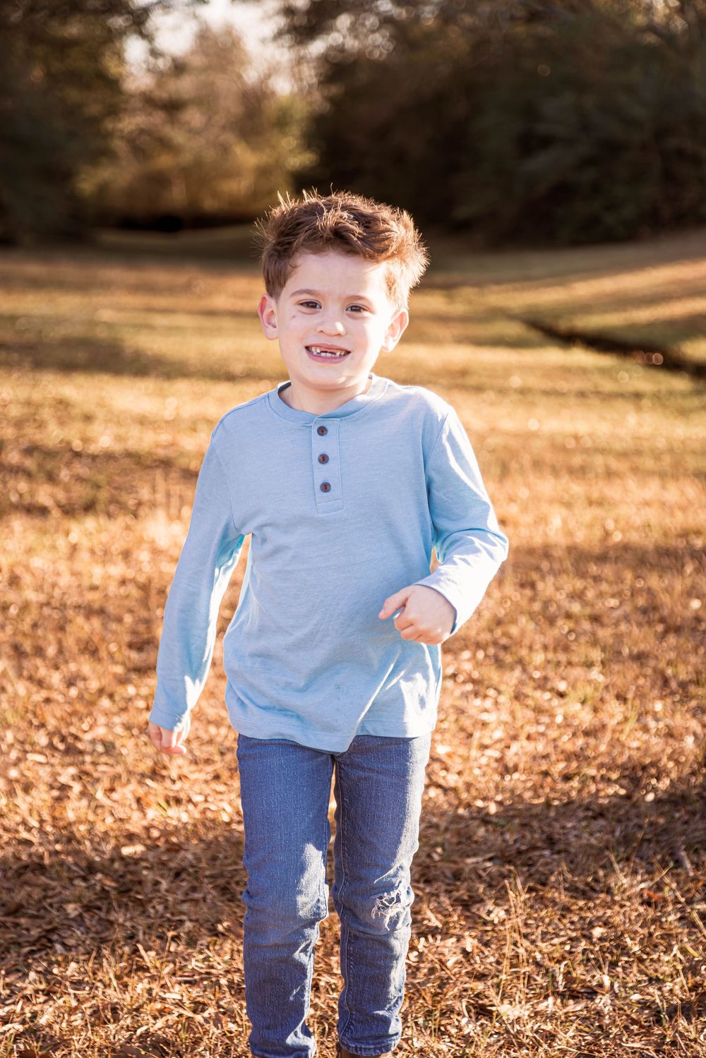 A child plays in fallen autumn leaves in a sunlit field during golden hour.