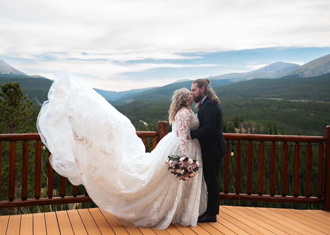Romantic mountain vista wedding portrait with flowing veil on wooden deck.