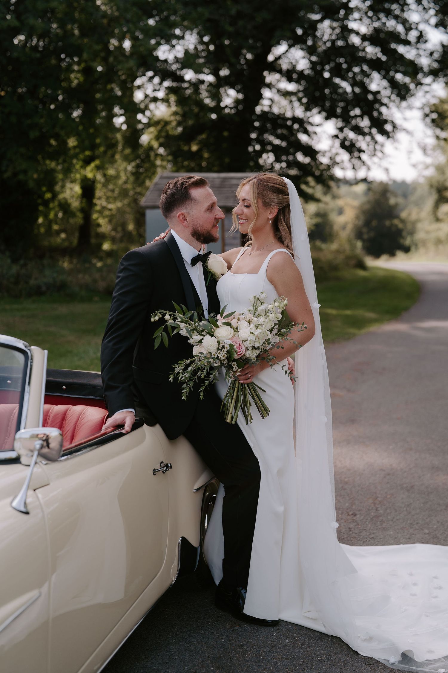 bride and groom leaning against wedding car at ivy lodge in cirencester