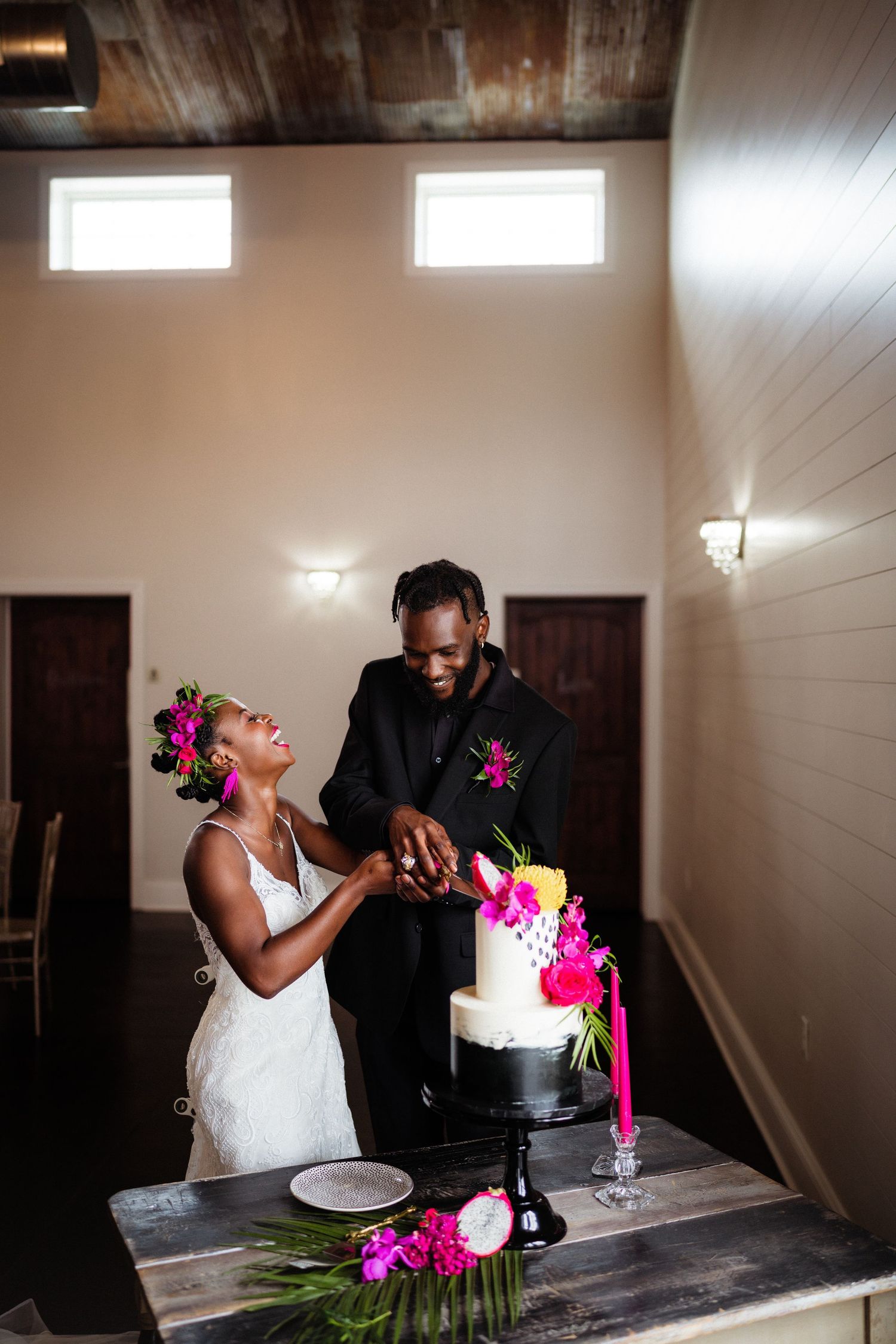 Bride and groom cut their decorated black and white wedding cake adorned with bright flowers.