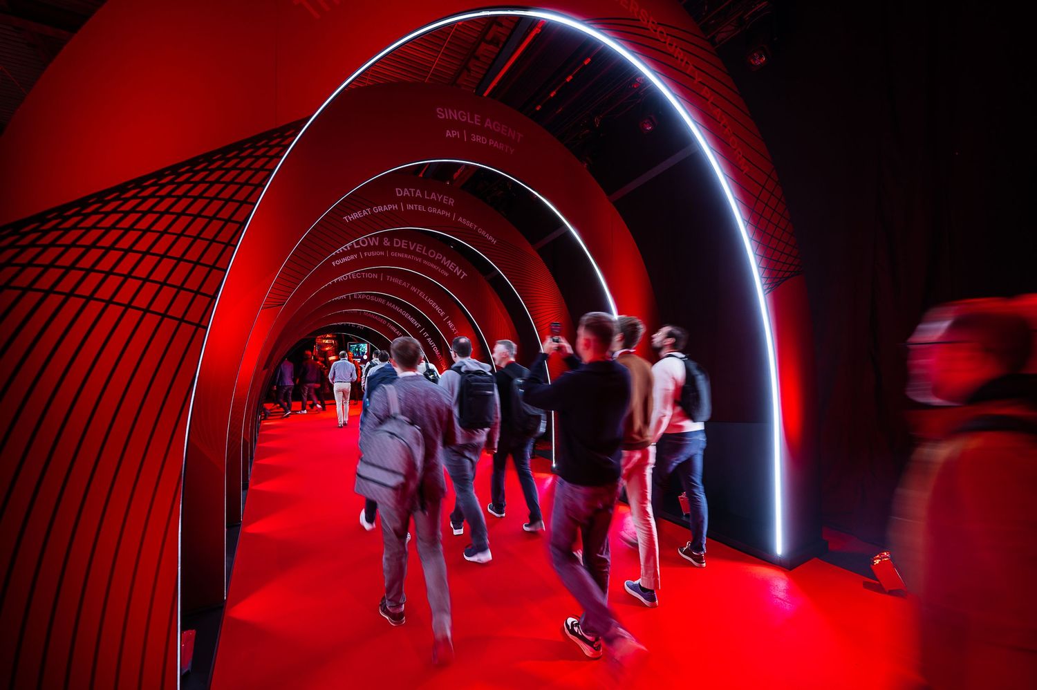 People walking through a glowing red-lit tunnel installation at an event.