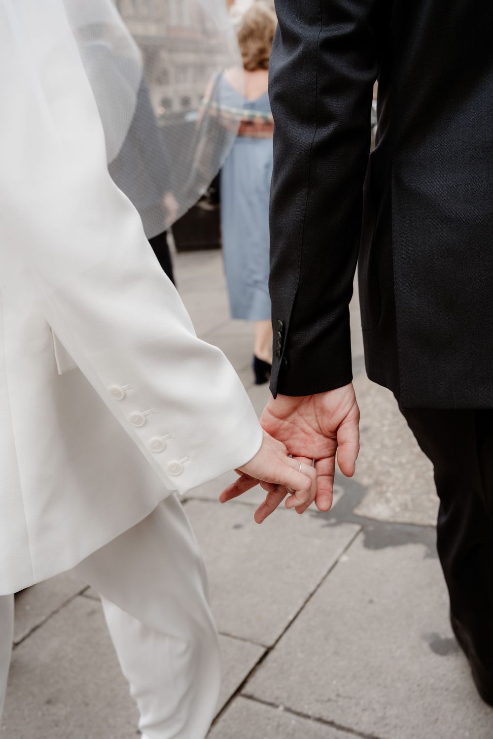Close-up shot of a couple holding hands, with one wearing a white dress and the other in a black suit.
