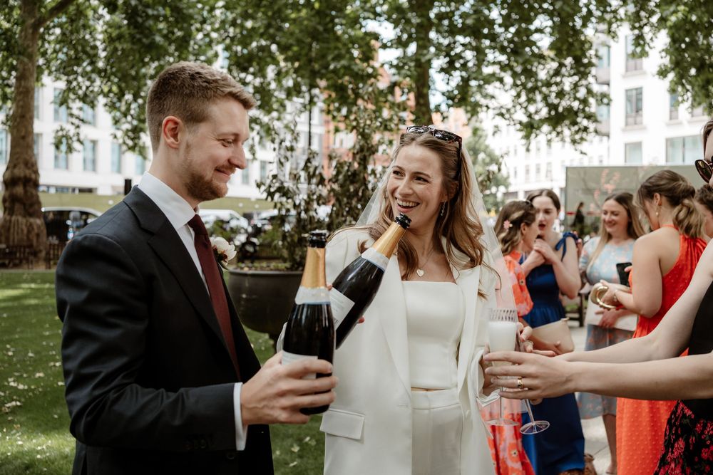 Wedding guests enjoy drinks and conversation during an outdoor cocktail reception at a garden venue.