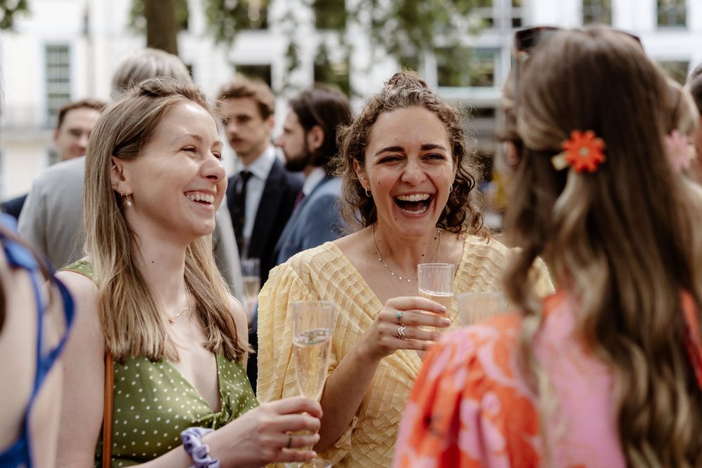A group of friends laughing and enjoying drinks at an outdoor social gathering on a sunny day.