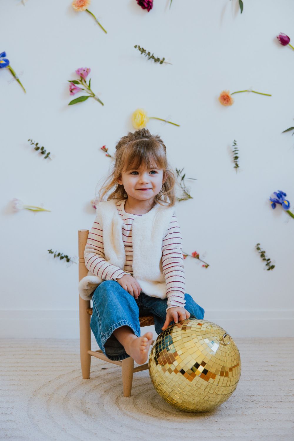 Colorful flower petals scattered on white surface with child sitting in wooden chair near woven basket.