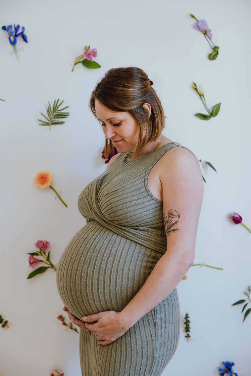Maternity photo series showing a pregnant woman in a green ribbed dress against a white background with scattered flowers.