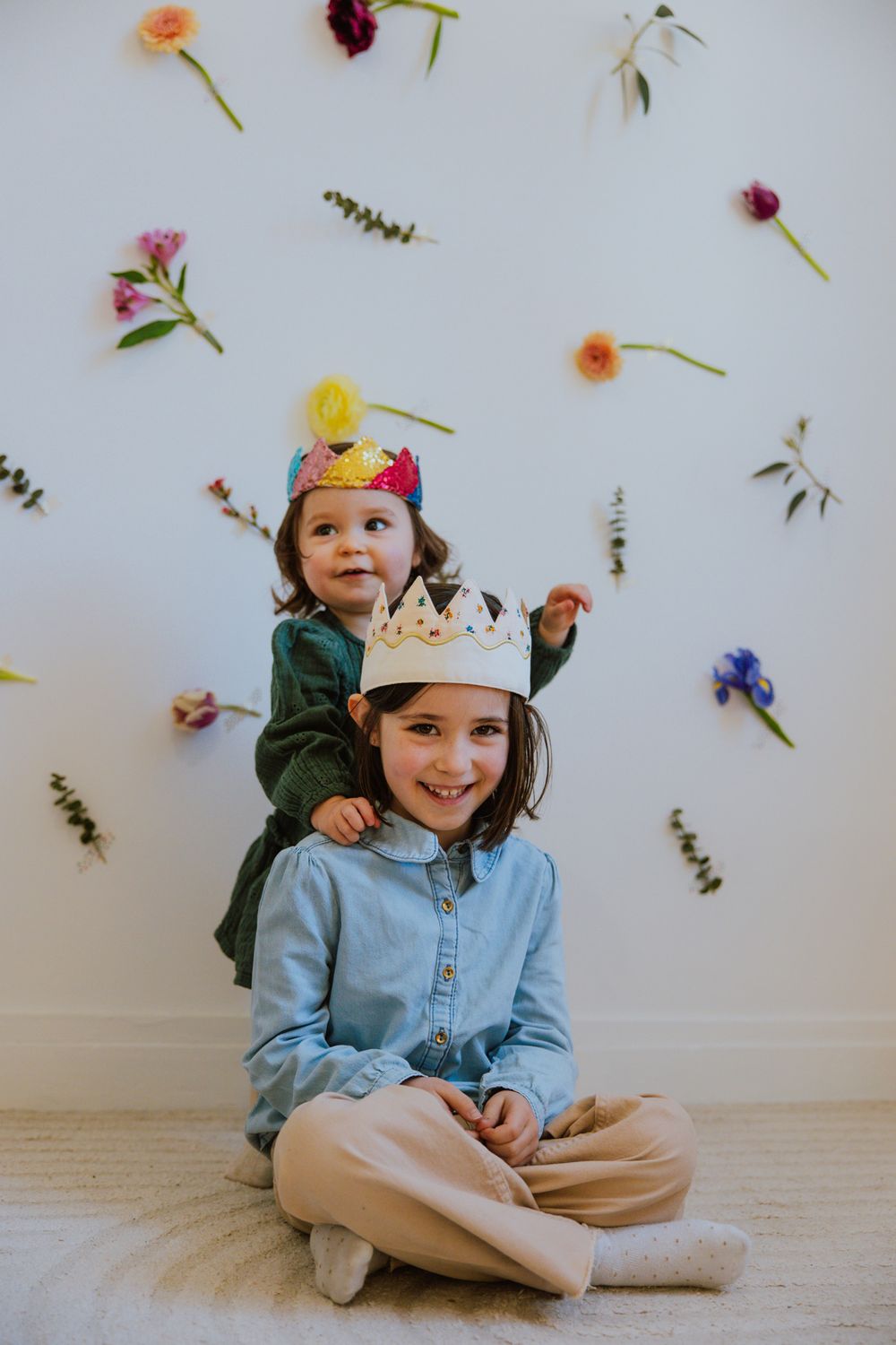 Playful scene with paper crowns against a wall decorated with scattered colorful flowers and greenery.
