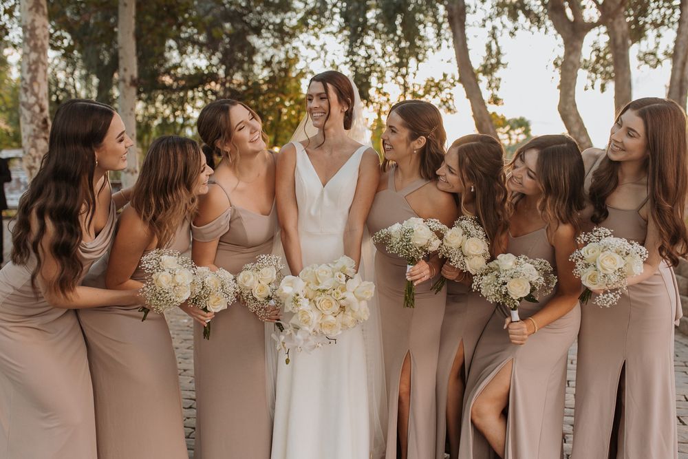 Wedding party in blush pink dresses holding white bouquets pose together outdoors at Lake Oak Meadows in Temecula.
