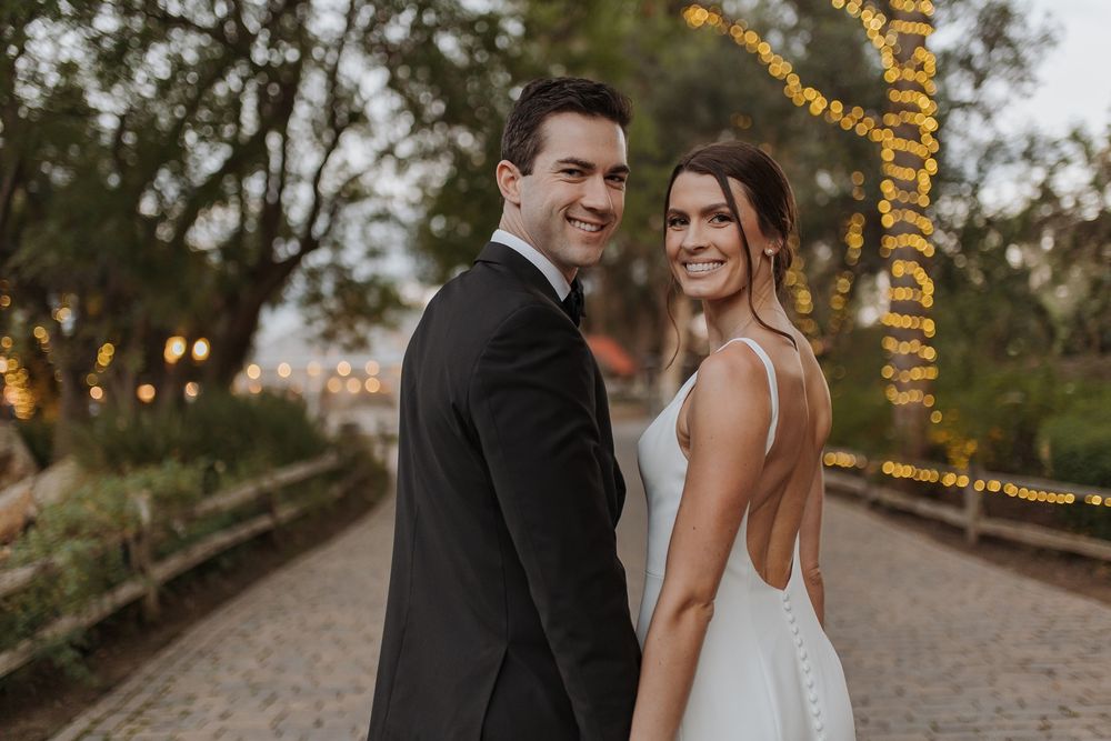 A romantic wedding photo series showing a couple sharing intimate moments on a tree-lined path at sunset at Lake Oak Meadows in Temecula.