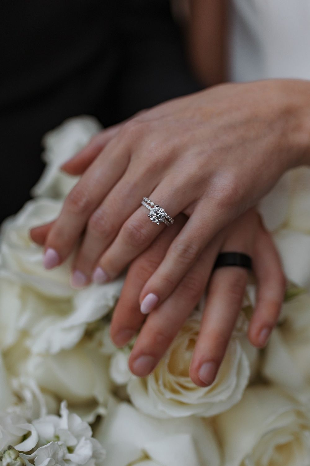 Close-up of sparkling engagement ring and wedding band on hand resting on white roses at Lake Oak Meadows in Temecula.