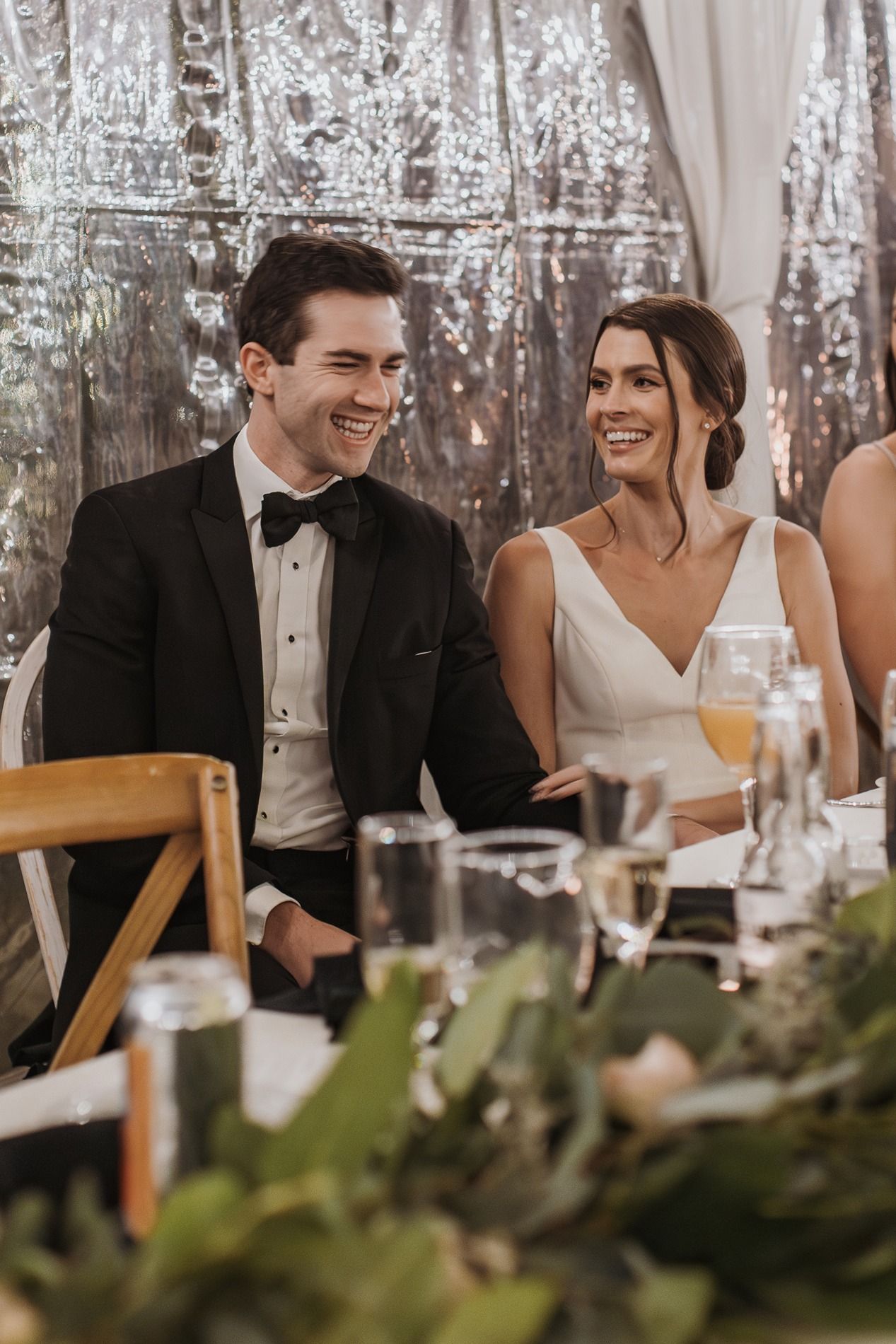A couple shares joyful laughter during an elegant wedding reception with greenery decor at Lake Oak Meadows in Temecula.