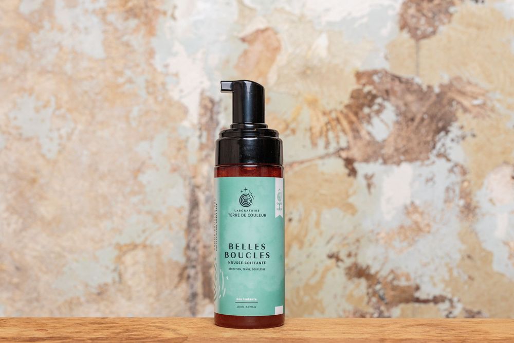 Belles Boucles curl-defining foam cleanser bottle with pump dispenser on wooden shelf.
