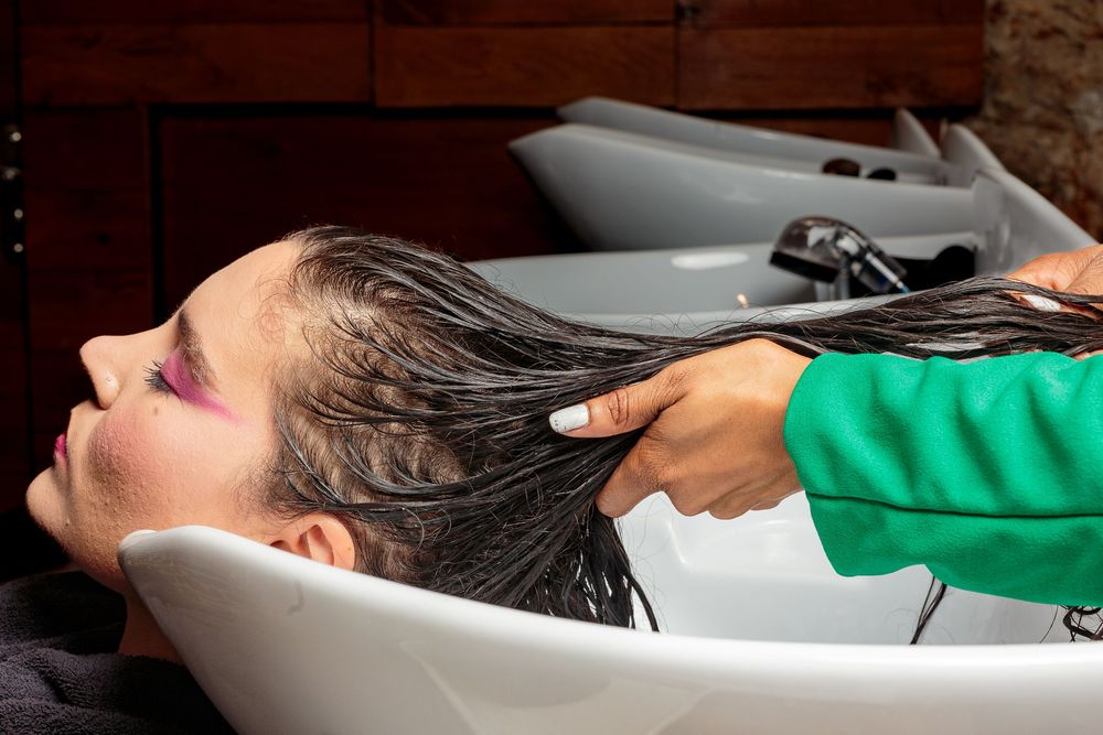 A hairstylist massages shampoo into a female clients wet hair at a salon washing basin.