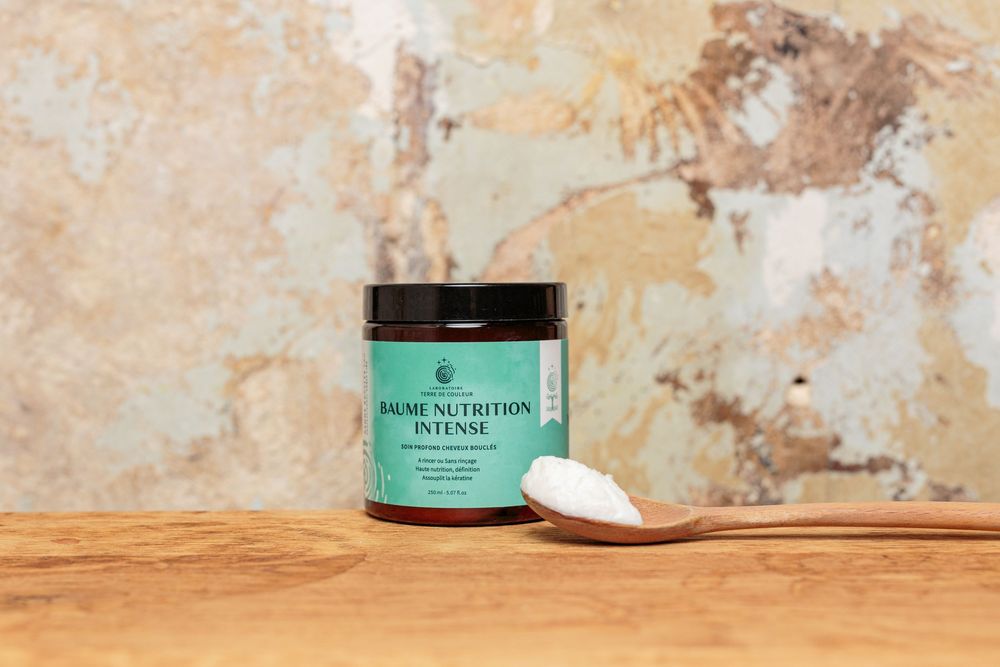 Baume Nutrition Intense deep conditioning hair balm jar with wooden spoon on table.