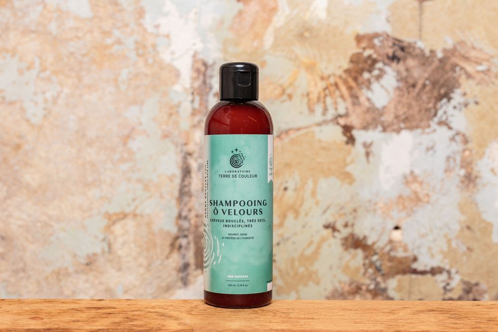 Shampooing Velours gentle natural shampoo bottle displayed on wooden surface against wall.