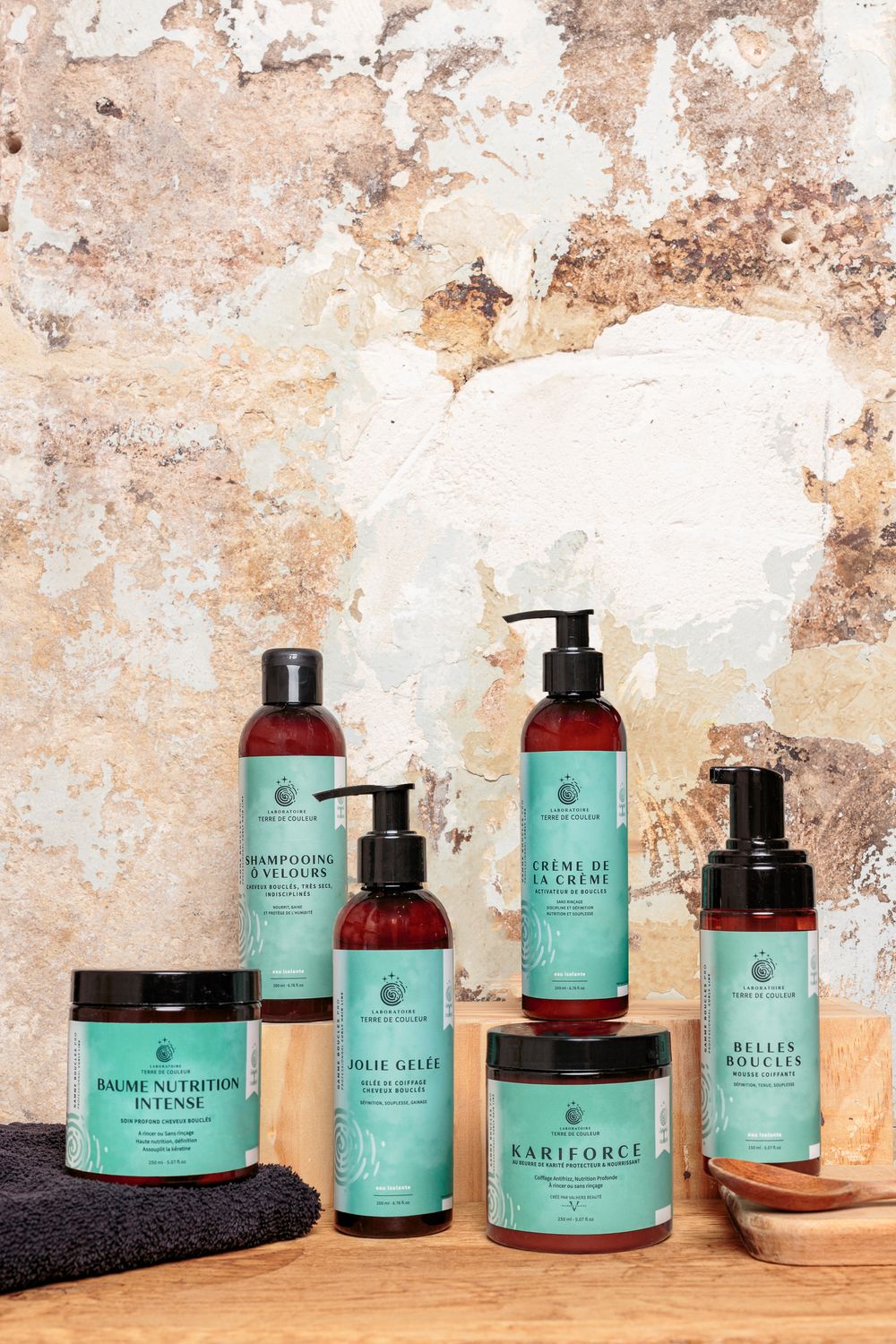 Collection of natural hair care products with teal labels arranged on a wooden surface against a rustic wall.