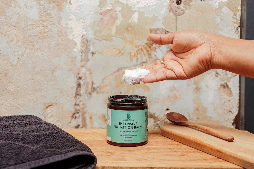 Hand scooping product from a teal-labeled intensive nutrition balm jar on a wooden surface.