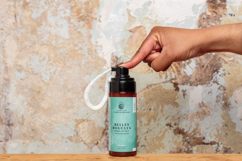 Hand pressing pump dispenser of Belles Boucles curl foam hair product bottle.