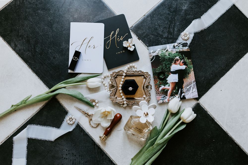 Wedding accessories including jewelry, fragrance, flowers and name cards arranged on a black and white geometric surface.