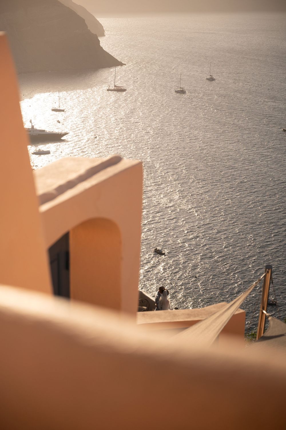 Peaceful view of sailboats on sparkling Mediterranean waters from a peach-colored architectural viewpoint in Santorini.