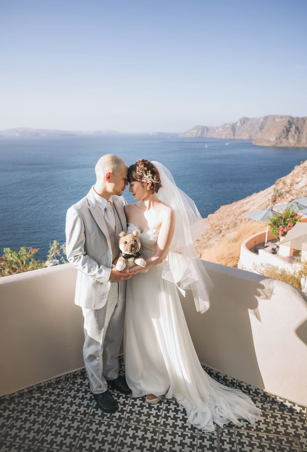 Wedding couple embraces on a terrace overlooking the Mediterranean cliffs and sea in Santorini, Greece.