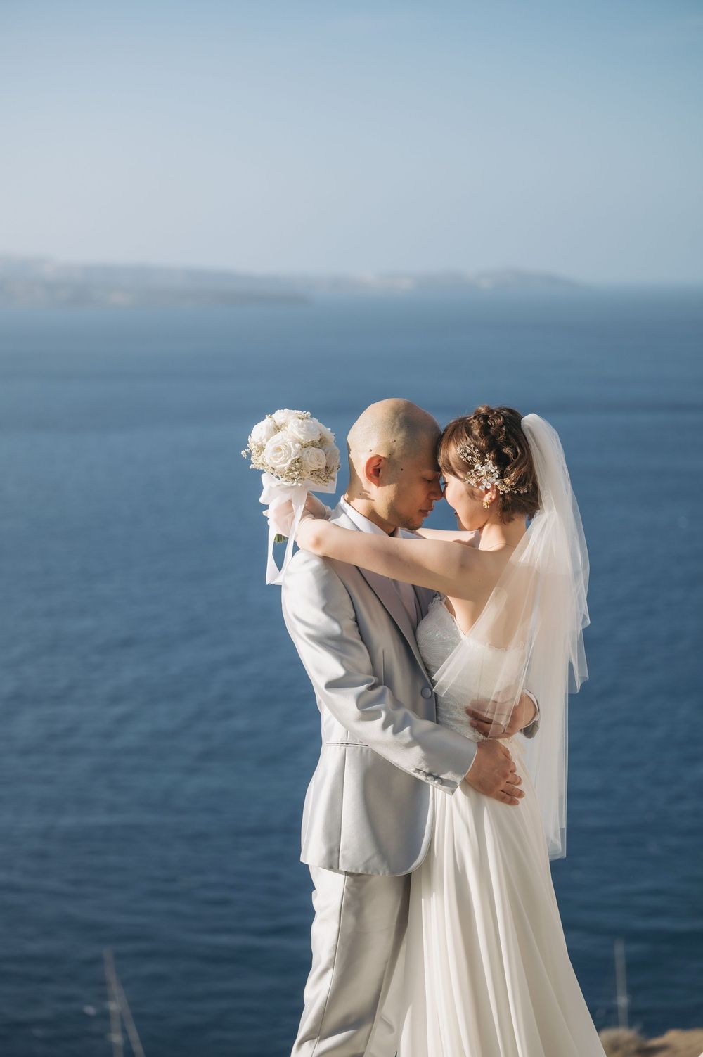 A romantic wedding moment captured against the blue Mediterranean Sea in Santorini.