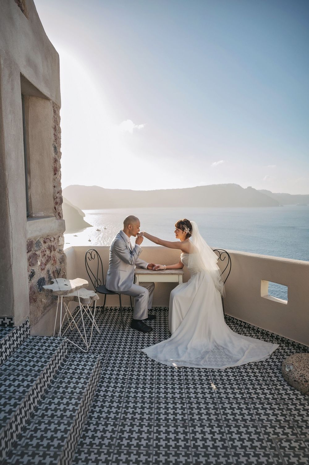 A wedding couple shares intimate moment at cafe table with stunning coastal views of Santorini.