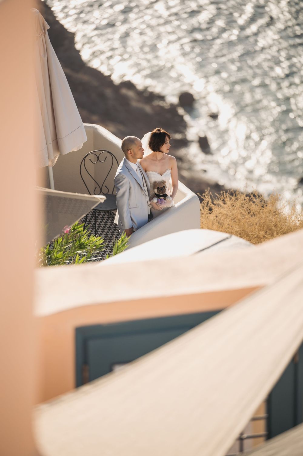 A romantic couple overlooks a scenic ocean view from a cliffside balcony in Mediterranean architecture.