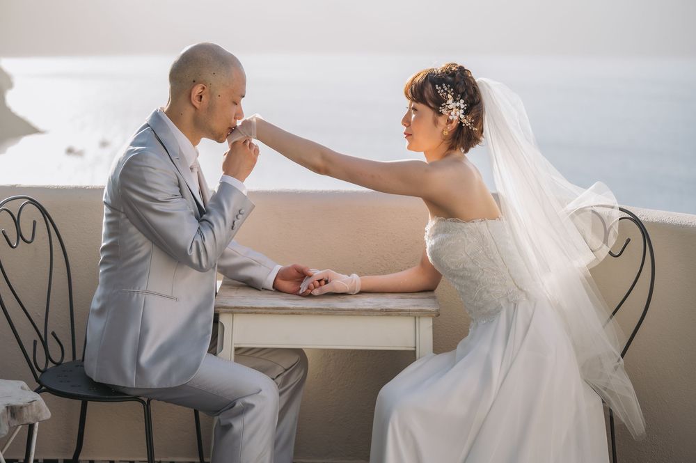 A tender moment between newlyweds at outdoor cafe table with Mediterranean backdrop.