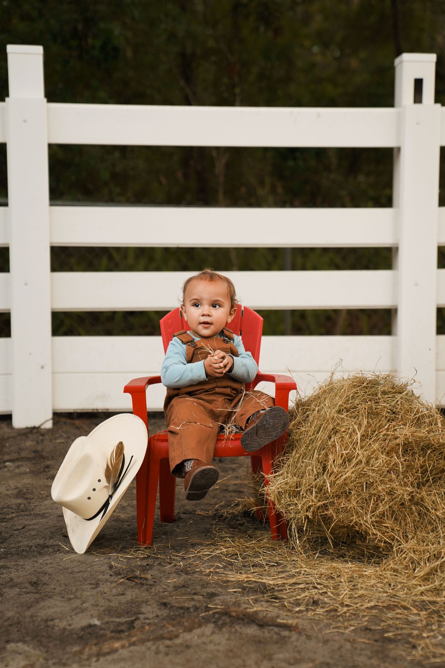 Baby in red gingham outfit plays with cake and icing during festive cake smash photo session.
