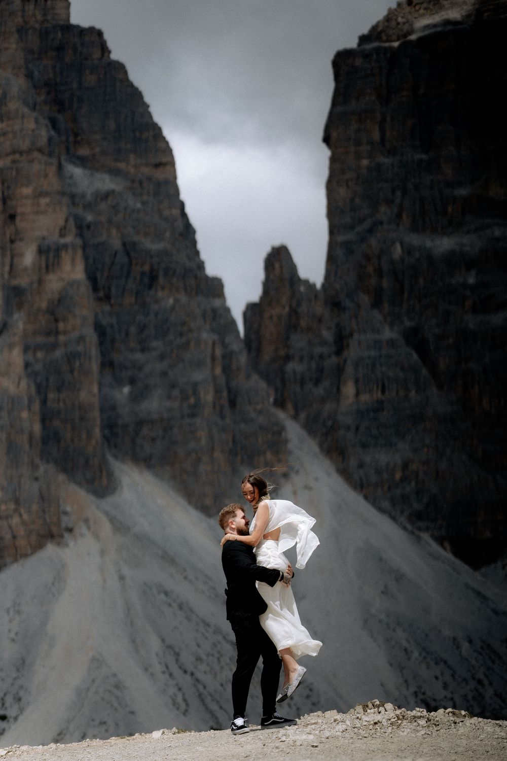 Bride and groom embrace between dramatic Dolomite mountain peaks on their wedding day.