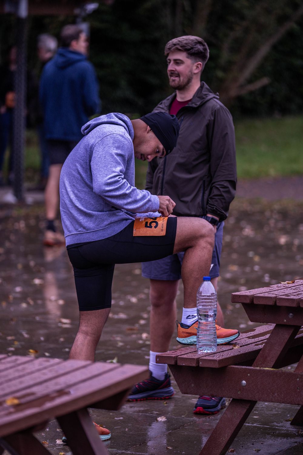 Two runners checking race numbers on wooden picnic bench before event.