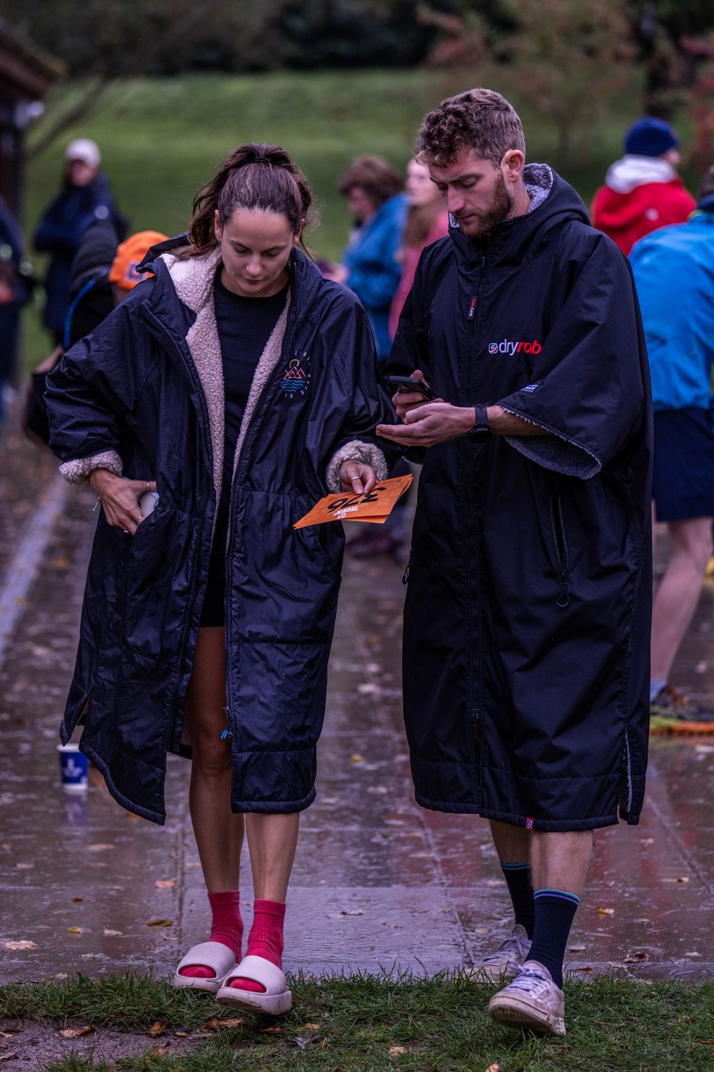 Two participants in rain coats checking race materials on wet pathway.
