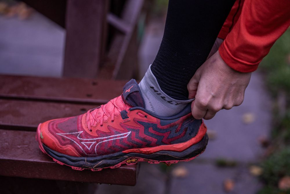 Close-up of red and black trail running shoe on wooden steps.