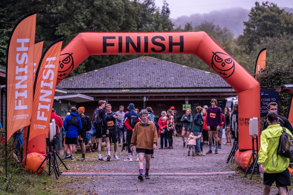 Runners gathering under an orange finish line arch at a trail race event.