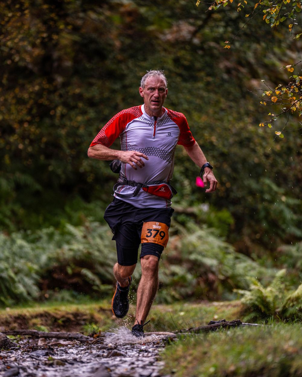 Trail runner splashing through water crossing during forest race.